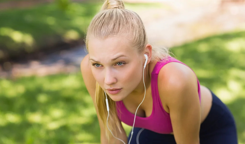 Junge Frau in Sportkleidung beugt sich erschöpft nach vorne